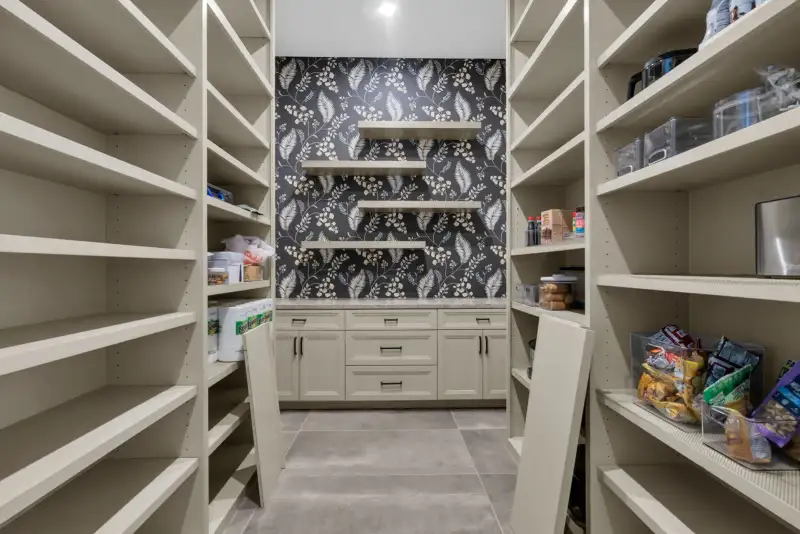 Pantry with open shelving on both sides and floral wallpaper on the back wall.