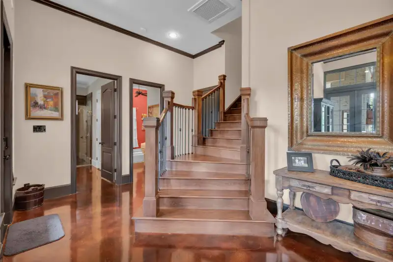 Hallway with a wood staircase and iron balusters, a framed mirror above a console table, and stained concrete floors.