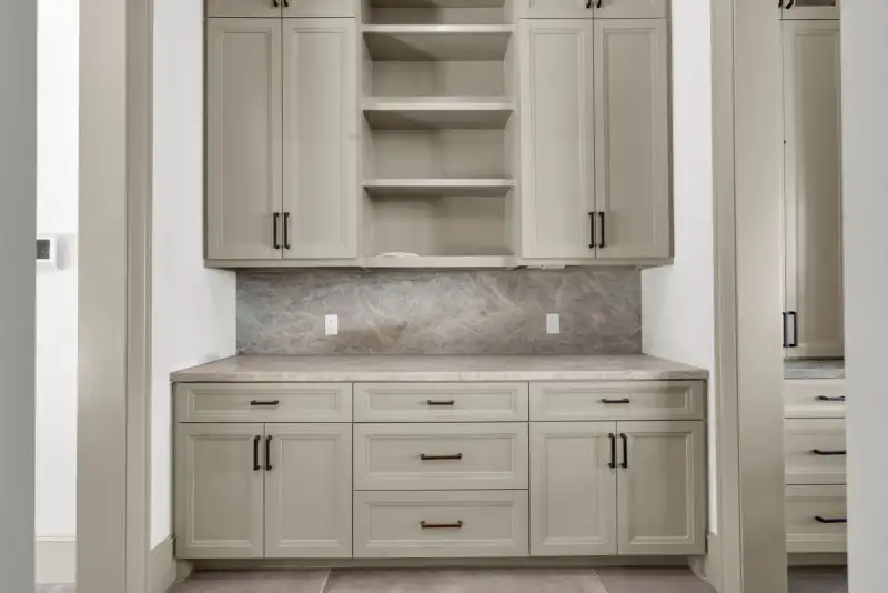 Cabinet wall with light upper and lower cabinets, a counter, and a stone backsplash.