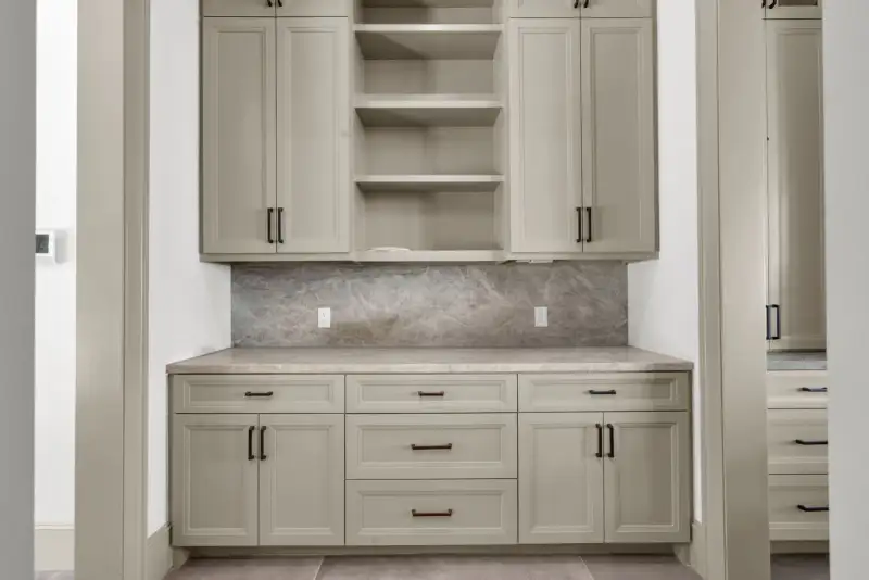 Cabinet wall with light upper and lower cabinets, a counter, and a stone backsplash.