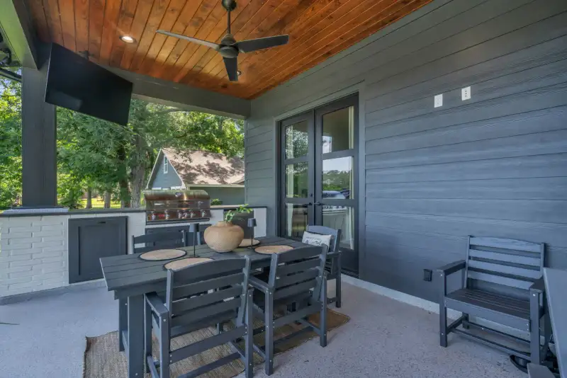Covered patio with a dark dining table, gray chairs, a ceiling fan, and a wood-paneled ceiling.