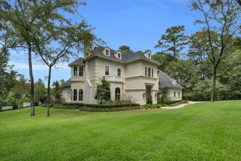 Front facade of a cream stucco home with arched windows, a curved walk, and clipped boxwood beds.