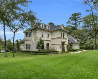 Front facade of a cream stucco home with arched windows, a curved walk, and clipped boxwood beds.