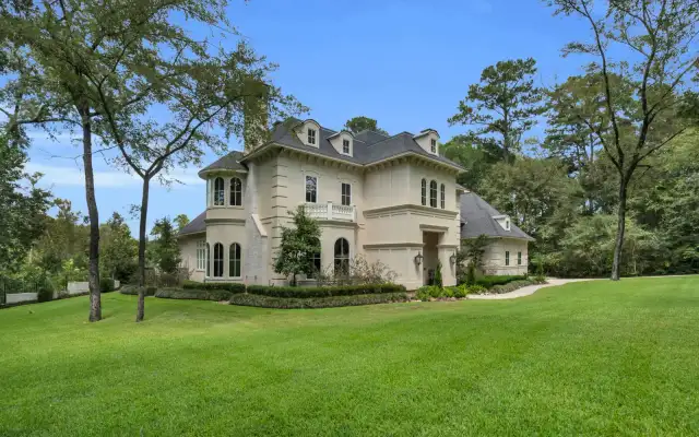 Front facade of a cream stucco home with arched windows, a curved walk, and clipped boxwood beds.