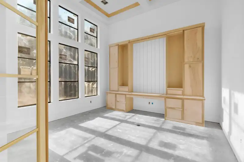 Unfinished room with built-in light wood cabinetry and a desk, tall windows, and a coffered ceiling.