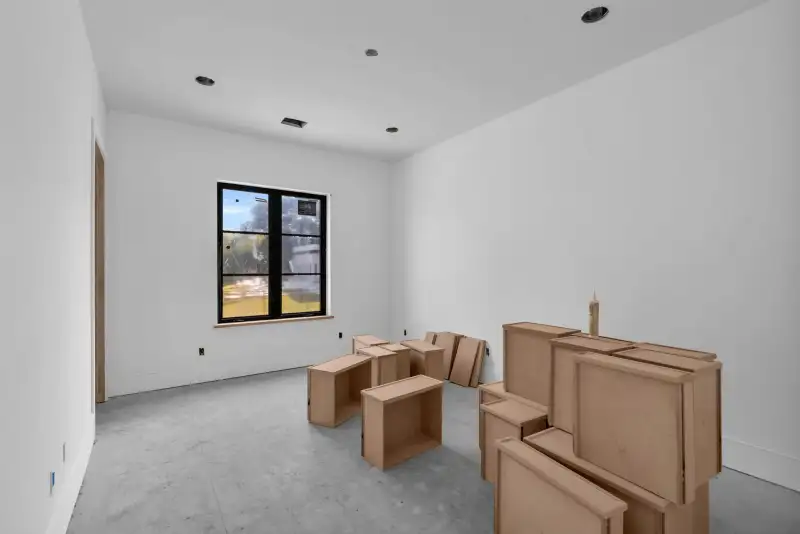 Empty room with white walls, recessed lights, and cardboard cabinet boxes stacked near a window.