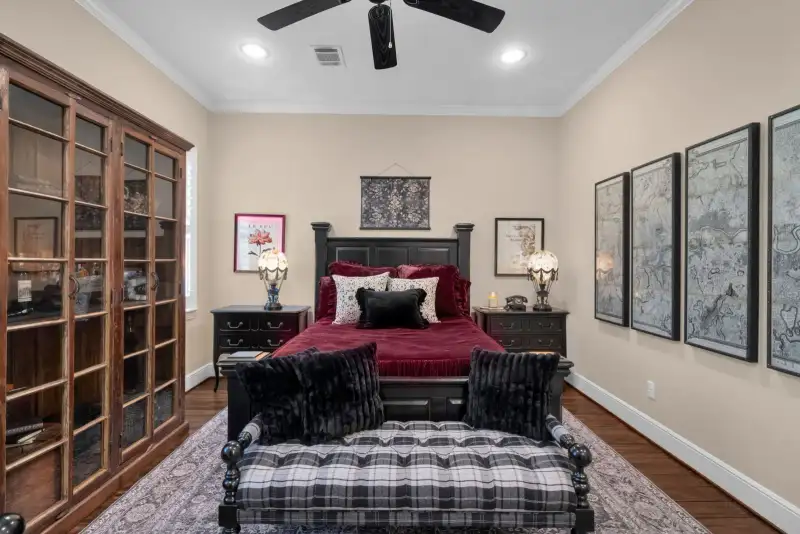 Bedroom with a black wood bed, red velvet bedding, a glass-front cabinet, and framed map prints on the wall.