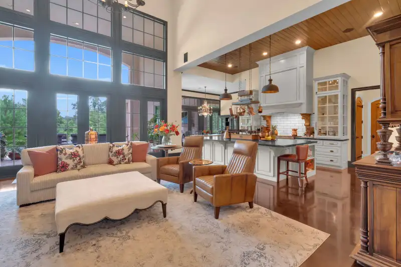 Open great room with divided-light windows, a wood-paneled ceiling, and a white kitchen island with pendant lights.