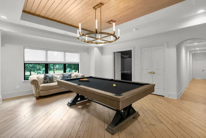 Game room with a pool table, a tan sofa beside a window, double doors, and an arched hallway.