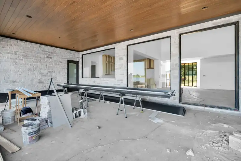 Covered patio with stone walls, a wood ceiling, and sliding glass doors, with a metal beam on sawhorses.