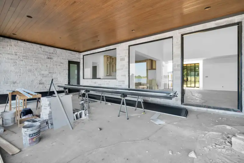 Covered patio with stone walls, a wood ceiling, and sliding glass doors, with a metal beam on sawhorses.