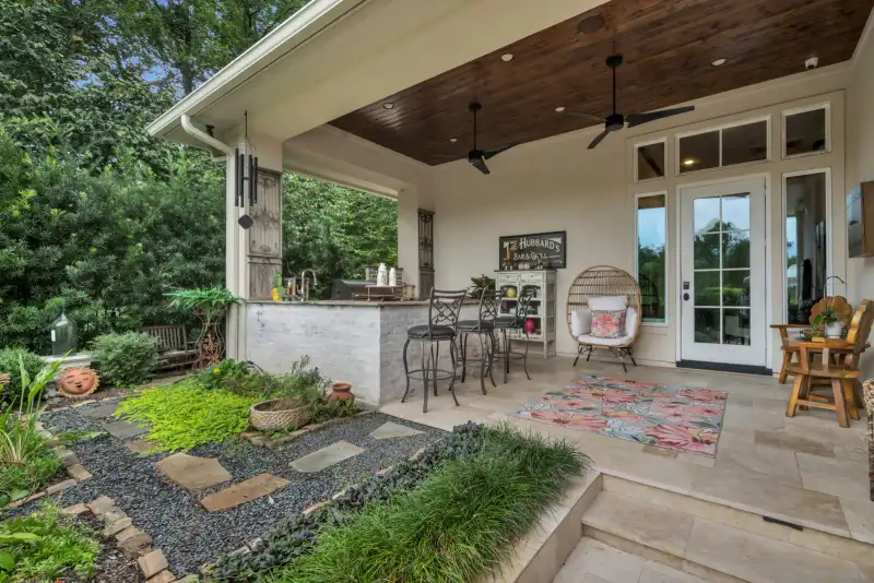 Covered outdoor bar with a stone counter, bar stools, a wood-planked ceiling, and a stone-lined garden path.