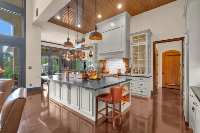 Kitchen with a dark island countertop, leather barstools, pendant lights, and glossy reddish-brown floors.