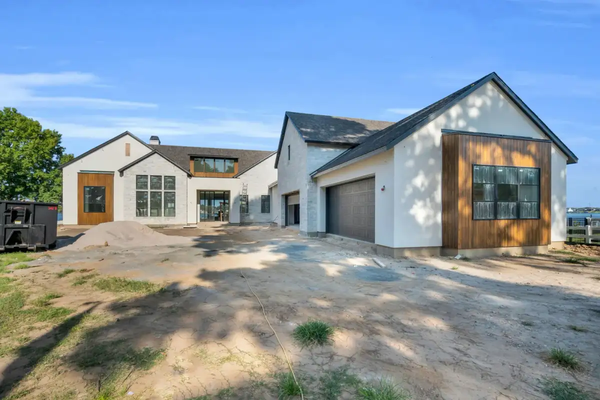 Front exterior of a stucco and stone house with wood accents and garage doors on a dirt drive.