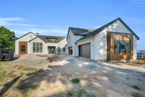 Front exterior of a stucco and stone house with wood accents and garage doors on a dirt drive.