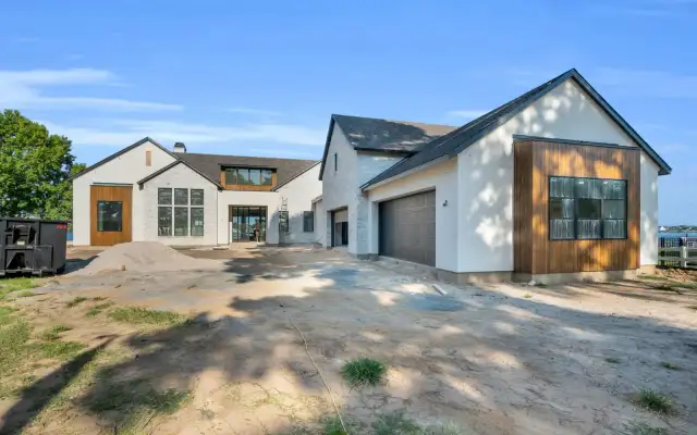 Front exterior of a stucco and stone house with wood accents and garage doors on a dirt drive.