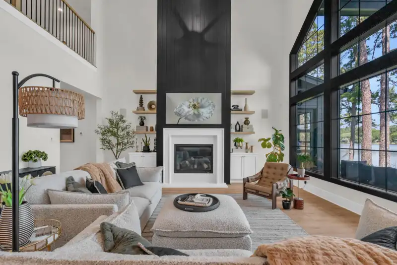 Living room with a white fireplace beneath a black shiplap wall, a gray sofa, and a large black-framed window.