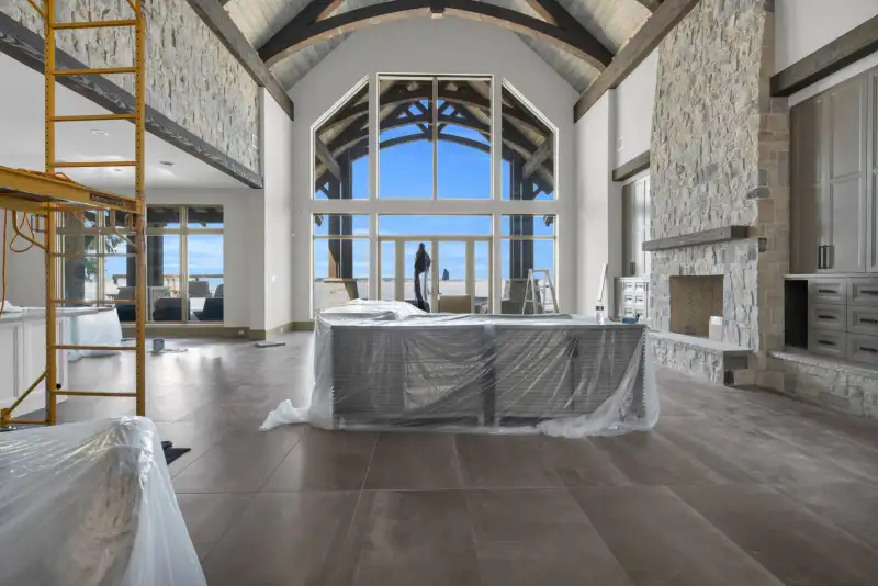 Two-story room with a stone fireplace, arched windows facing the water, and covered furniture.