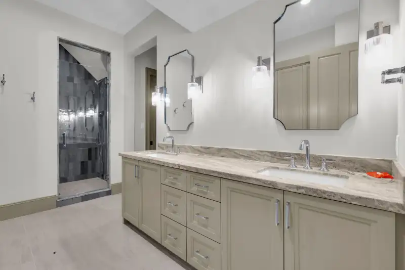 Bathroom with a double vanity, veined stone countertop, and a tiled shower at left.