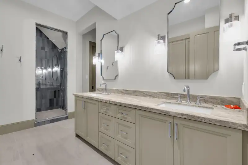 Bathroom with a double vanity, veined stone countertop, and a tiled shower at left.