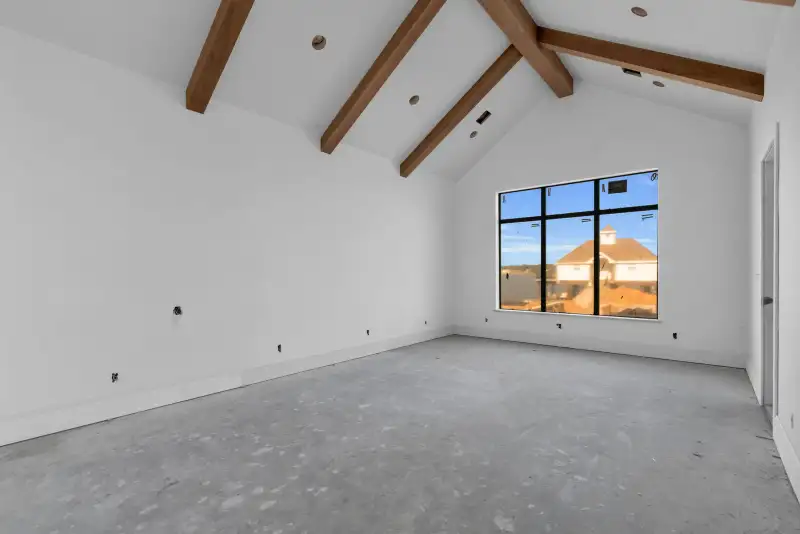 Vaulted room with exposed wood beams, a black-framed window, and bare concrete floors.