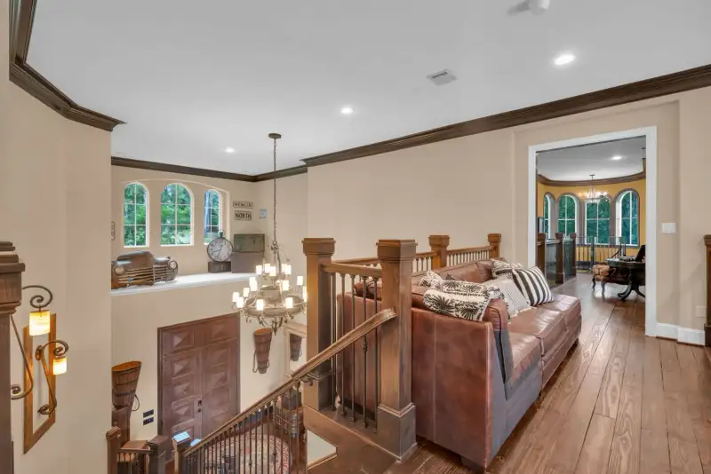Upper landing with a brown leather sofa, wood and iron balusters, a chandelier, and a view down to the foyer.