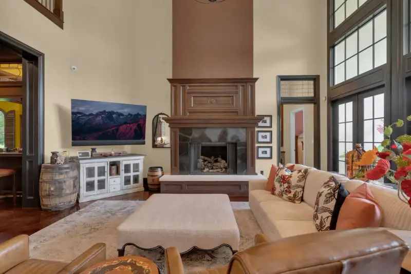 Living room with a wood-surround fireplace, a wall-mounted television, a cream sofa, and tall windows.