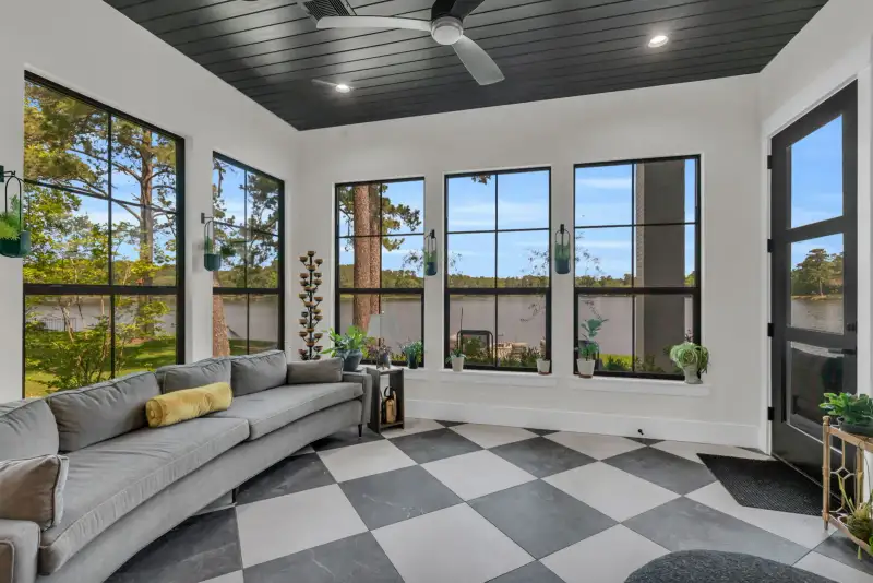 Sunroom with a curved gray sofa, black-framed windows, a checkered tile floor, and a dark plank ceiling.