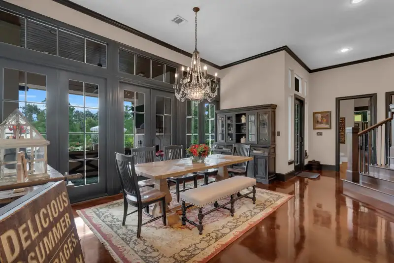 Dining room with a wood table, upholstered bench, crystal chandelier, dark French doors, and a dark china cabinet.