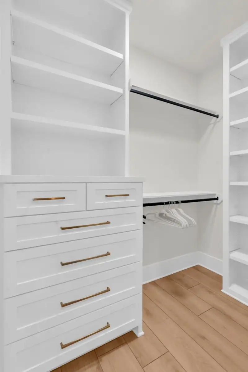 Walk-in closet with white built-in shelving, a hanging rod, and a chest of drawers with brass pulls.