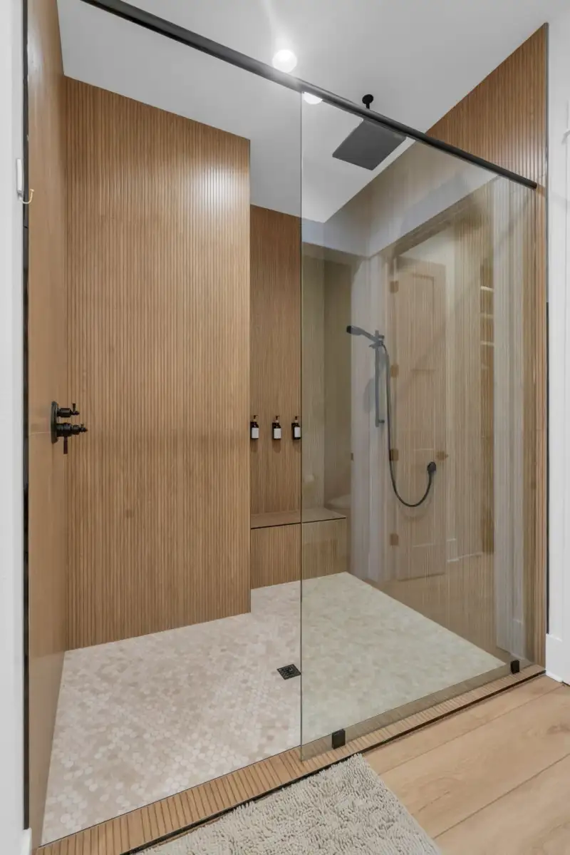 Walk-in shower with fluted wood wall panels, a glass enclosure, and small hexagonal floor tile.