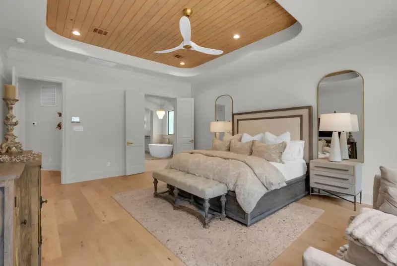 Bedroom with a wood plank tray ceiling, a bed with an upholstered bench, and a doorway to the bathroom.