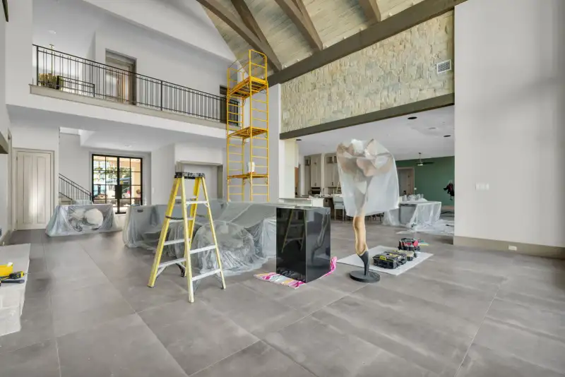 Open room with a balcony railing above, a stone wall, and a yellow scaffold tower.