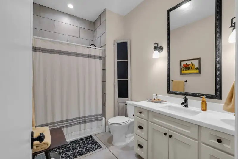 Bathroom with a gray tile shower, a striped shower curtain, a white vanity, and a framed mirror.