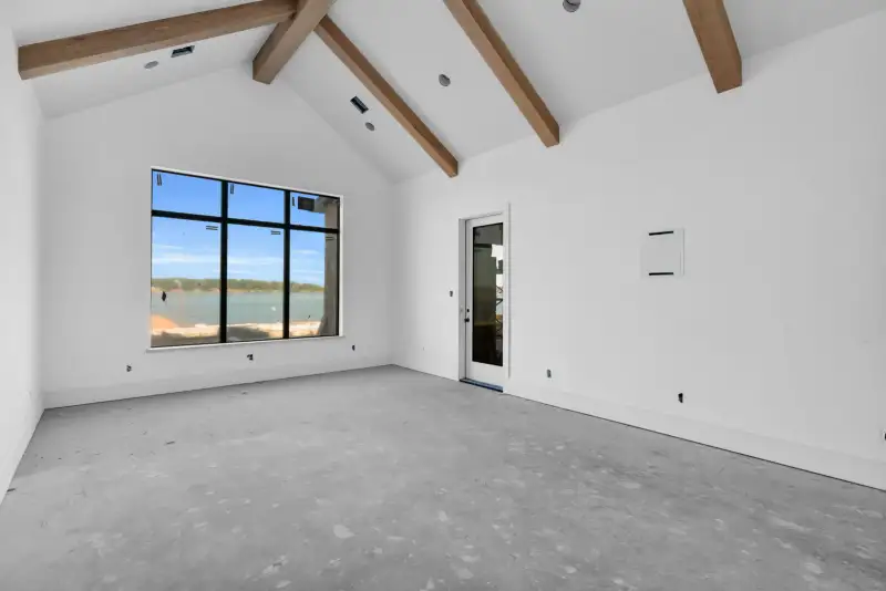 Vaulted room with exposed beams and a black-framed window looking out over water.