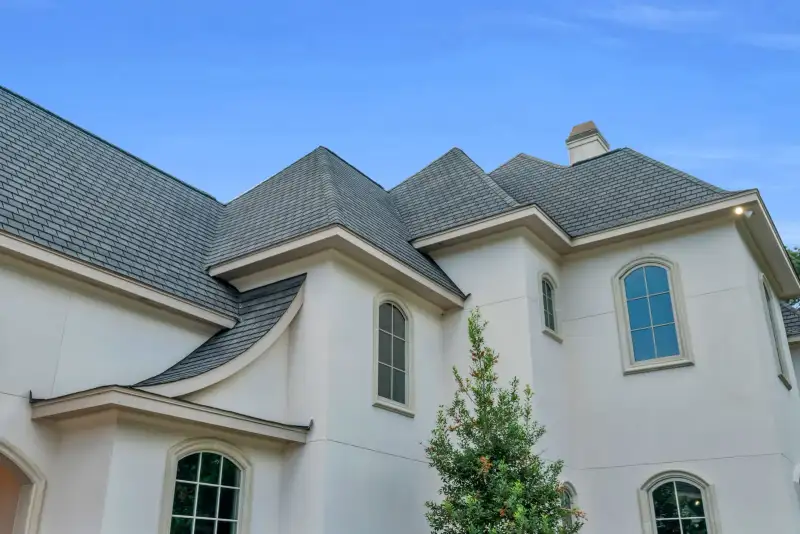 Roofline of a stucco home with gray roof planes, arched windows, and a chimney.