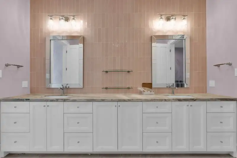 Double vanity with white cabinets, a veined stone countertop, and vertical pink tile behind the mirrors.
