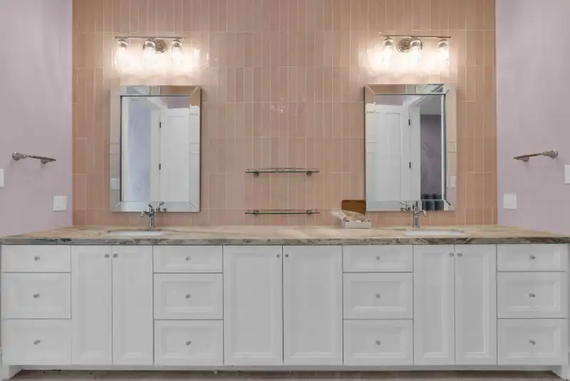 Double vanity with white cabinets, a veined stone countertop, and vertical pink tile behind the mirrors.