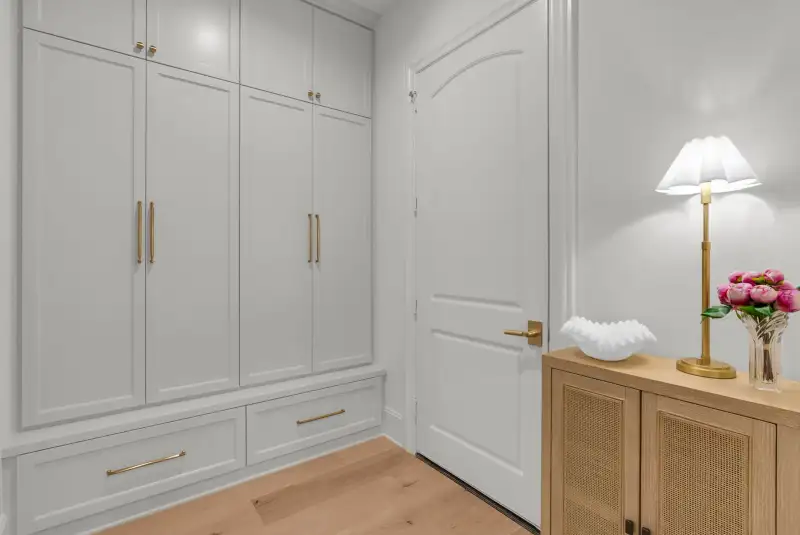 Built-in gray lockers with brass pulls beside a wood cabinet with cane-front doors and a table lamp.