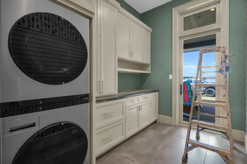 Laundry room with a stacked washer and dryer, light cabinets, and a green accent wall.