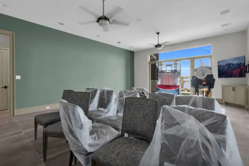 Family room with a green accent wall, dining chairs under plastic, and a wall-mounted TV.
