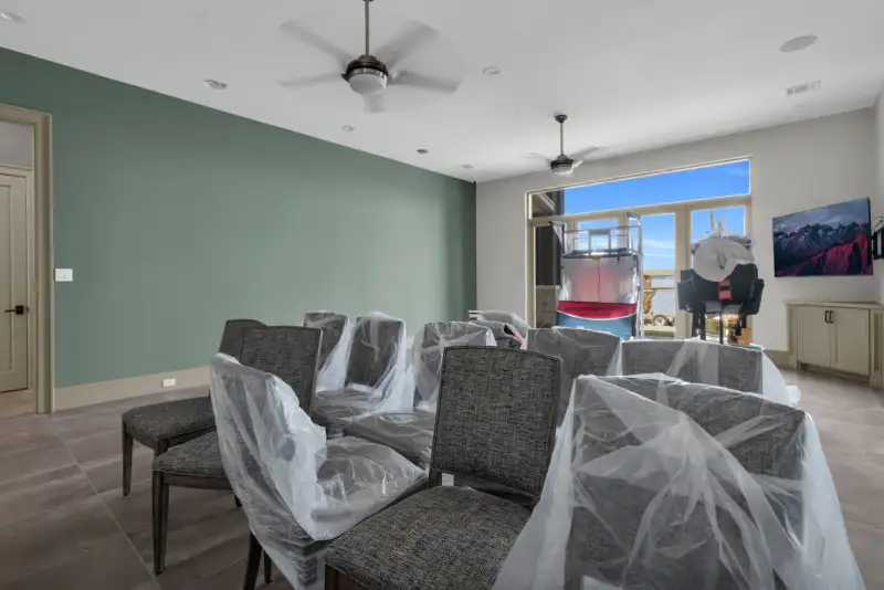 Family room with a green accent wall, dining chairs under plastic, and a wall-mounted TV.