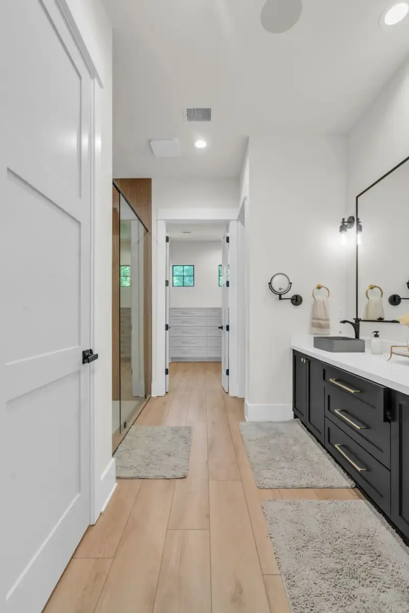Bathroom hallway with a black double vanity, gray vessel sinks, and a glass shower enclosure beside it.