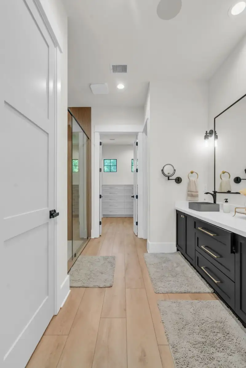 Bathroom hallway with a black double vanity, gray vessel sinks, and a glass shower enclosure beside it.