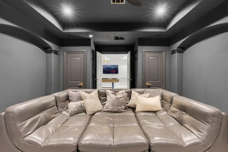 Home theater with a leather sectional, gray walls, and an open doorway to a hallway.