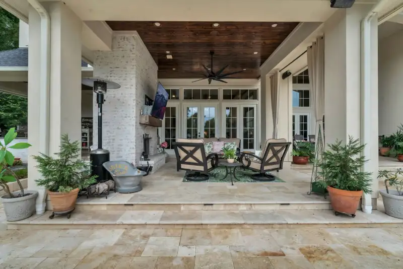 Covered patio with a brick fireplace, a wood-planked ceiling, a ceiling fan, and outdoor lounge chairs.