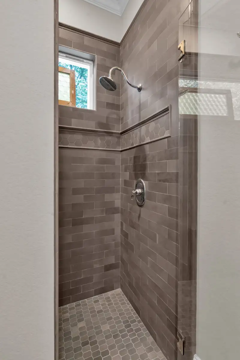 Shower with brown subway tile walls, a pebble-tile floor, and a handheld showerhead.