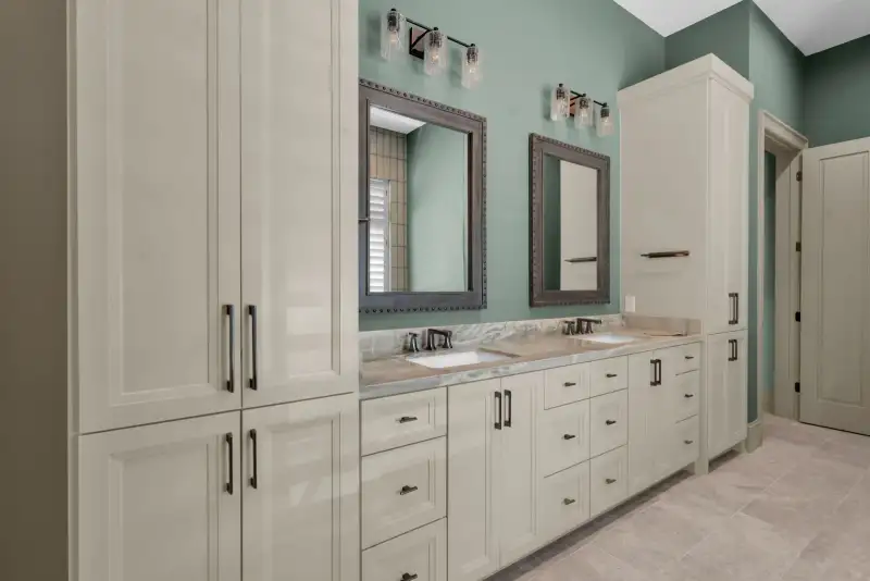Bathroom with a double vanity, cream cabinets, and green walls with two framed mirrors.