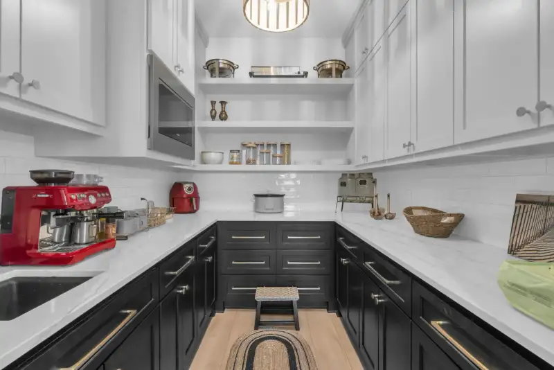 Pantry with dark lower cabinets, white upper cabinets, marble-look countertops, and open shelving.