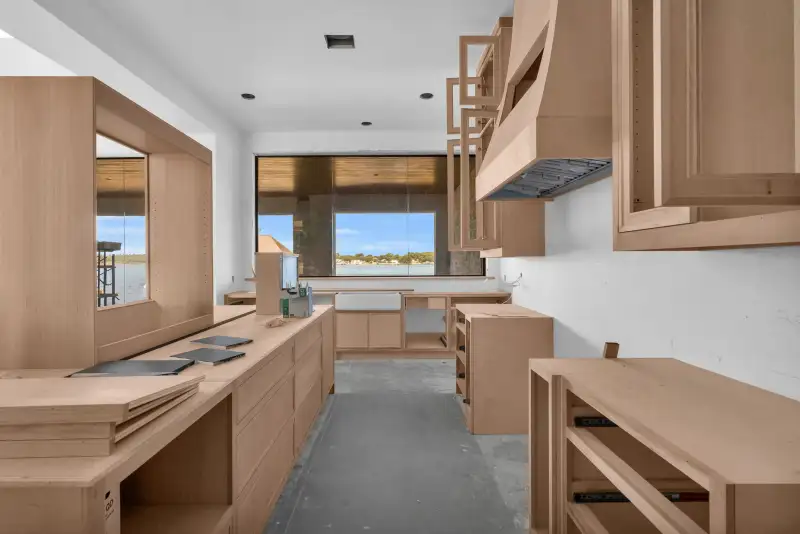 Narrow kitchen with a range hood, wood cabinets, and a window at the end showing water and trees.